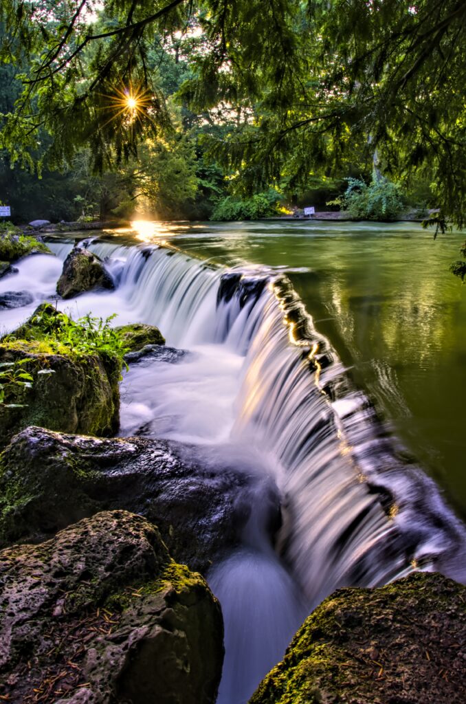 Serene waterfall over mossy rocks at sunrise with lush green forest and gentle river wallpaper