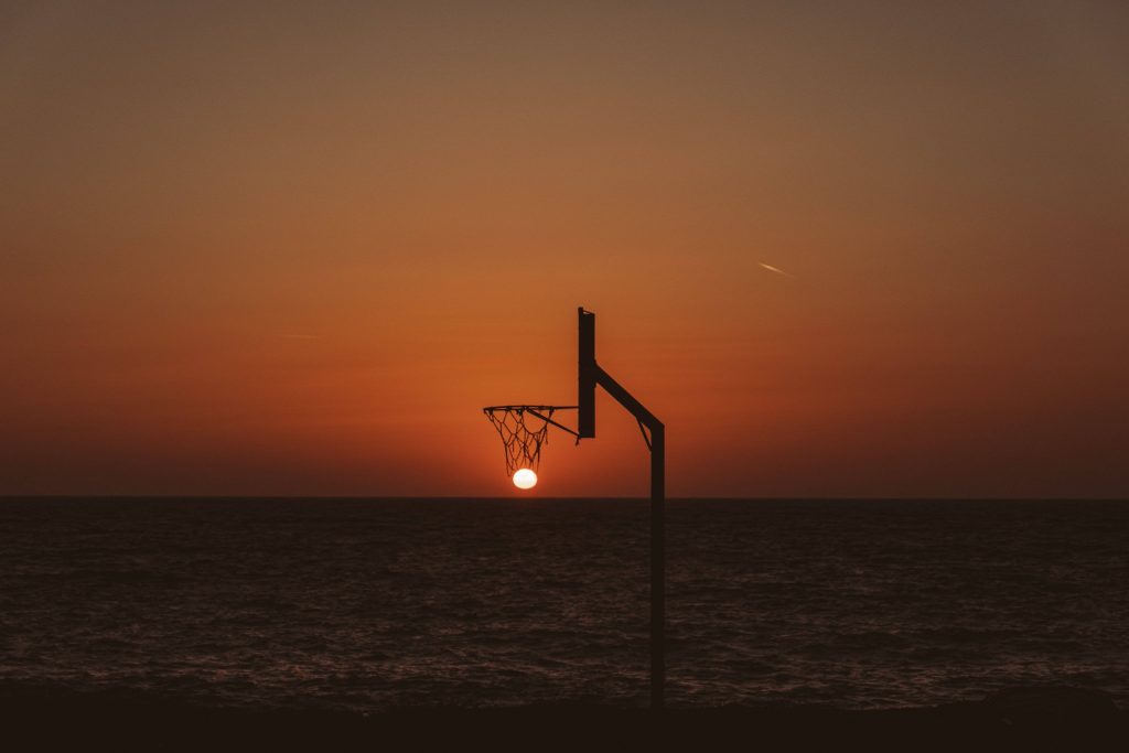 Basketball hoop silhouette framing sunset over calm ocean minimalist serene wallpaper background