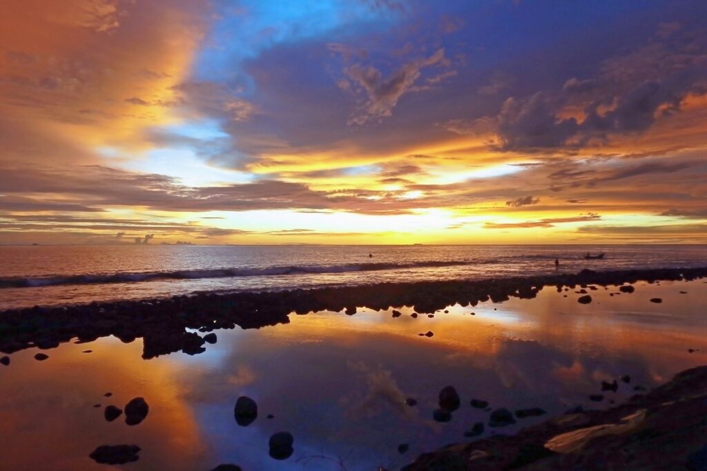 Sunset beach wallpaper with vibrant orange yellow blue sky reflecting calm water and dark rocks