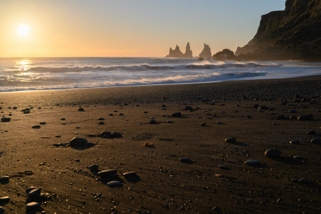 Serene sunset beach with smooth pebbles dark sand gentle waves and dramatic rock formations Wallpaper
