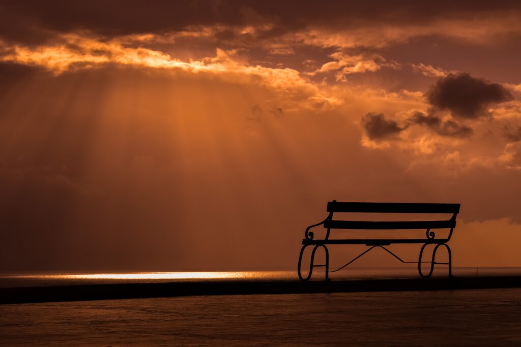 Solitary bench overlooking serene sunset with golden rays piercing dramatic clouds wallpaper
