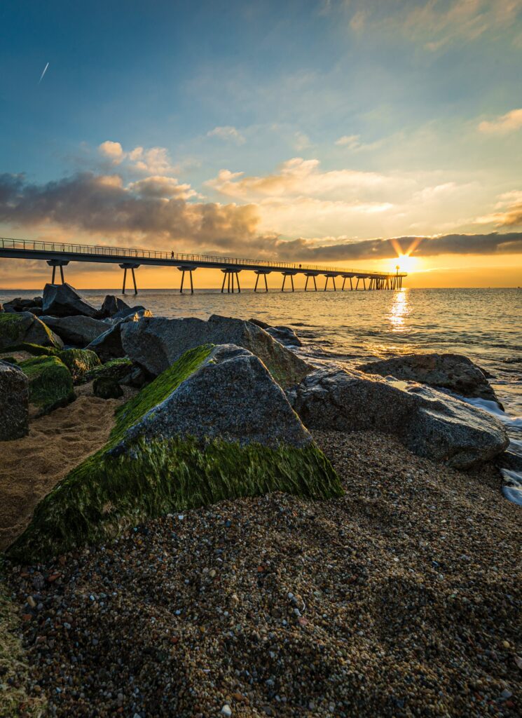 Sunset over calm ocean with long bridge mossy stones warm sunlight serene landscape wallpaper