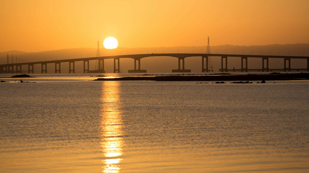 Sunset bridge over calm sea with golden light and serene natural beauty wallpaper background