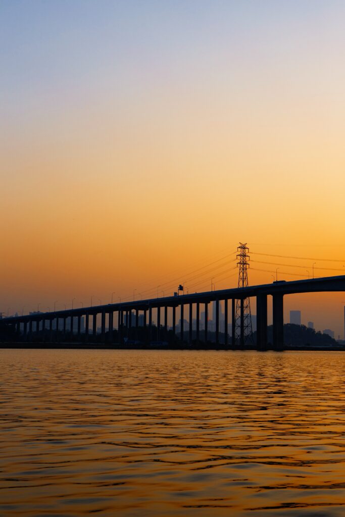Minimalist sunset wallpaper of a long bridge silhouette over calm water with warm orange hues
