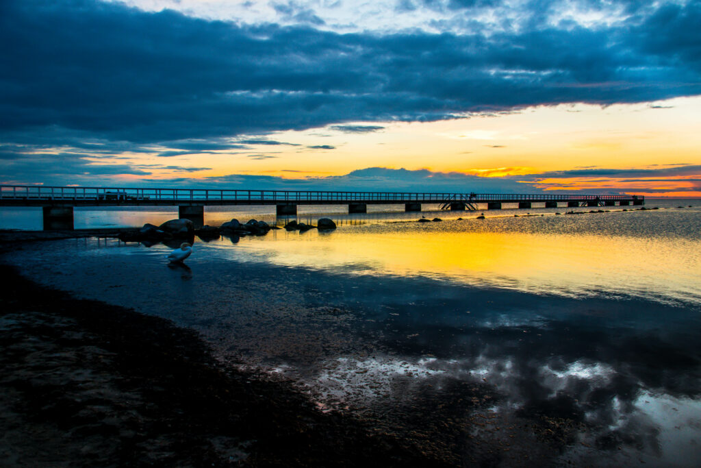 Long bridge over calm water at sunset with dramatic clouds and golden blue reflections wallpaper