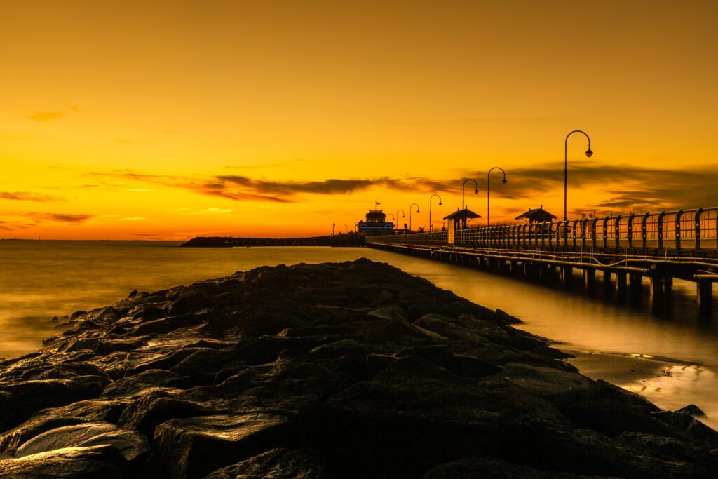 Serene sunset wallpaper with illuminated long bridge over calm waters and rocky path ahead