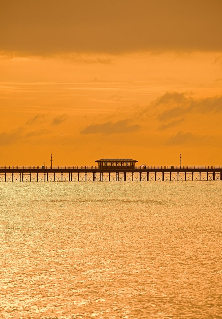 Serene bridge over shimmering water at sunset with warm orange hues and soft lens flare background Wallpaper