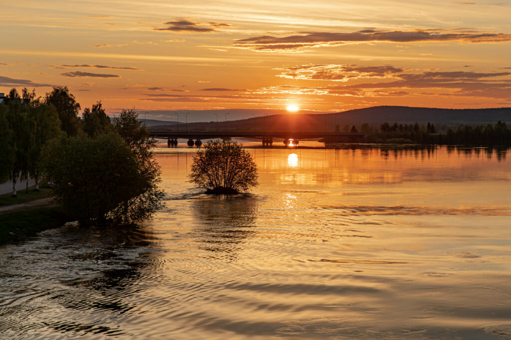 Serene sunset over calm water with golden rays bridge silhouette and peaceful nature background Wallpaper