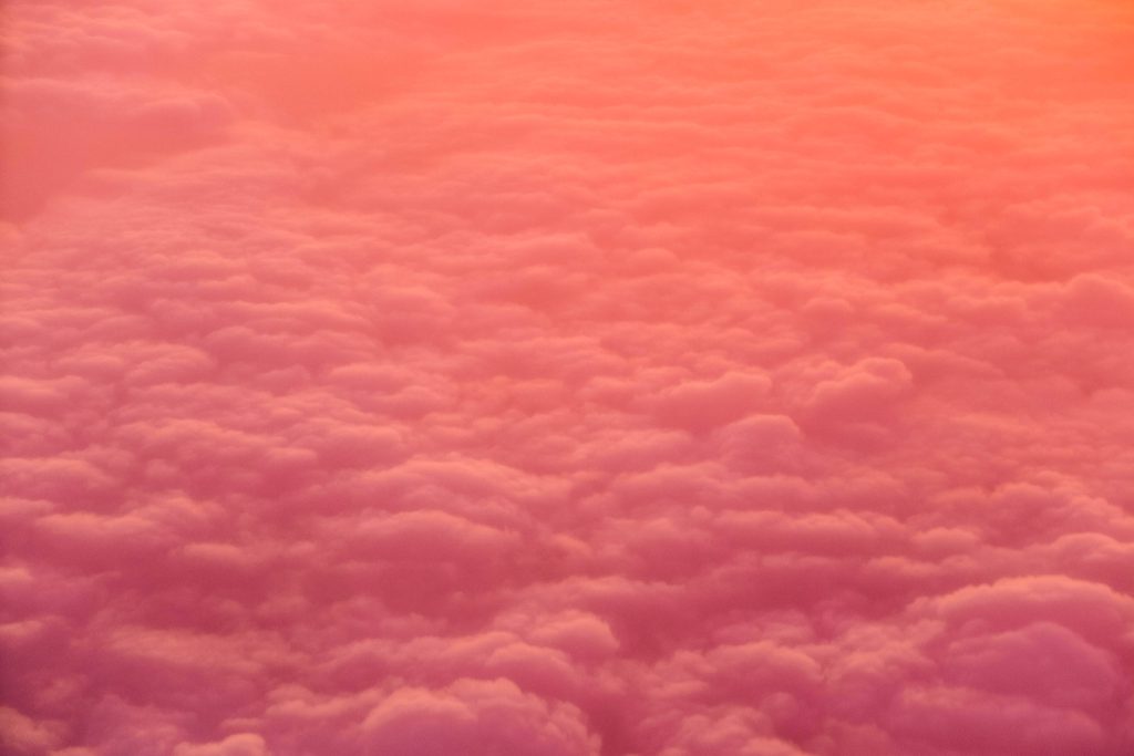 Aerial view of soft fluffy clouds glowing warm orange pink at sunset serene minimalist wallpaper