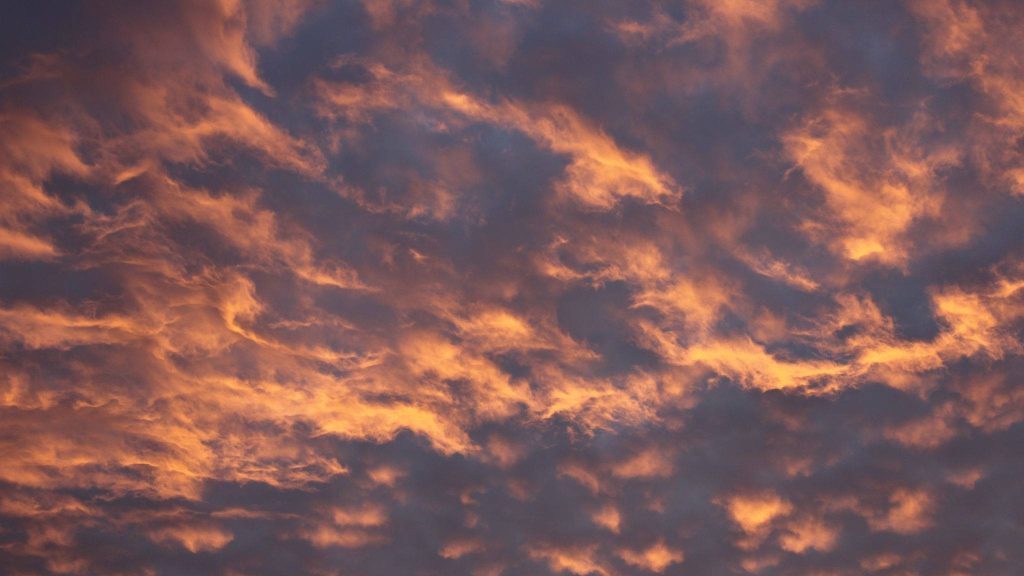 Sunset sky with dramatic golden orange clouds and deep charcoal grey shadows wallpaper background
