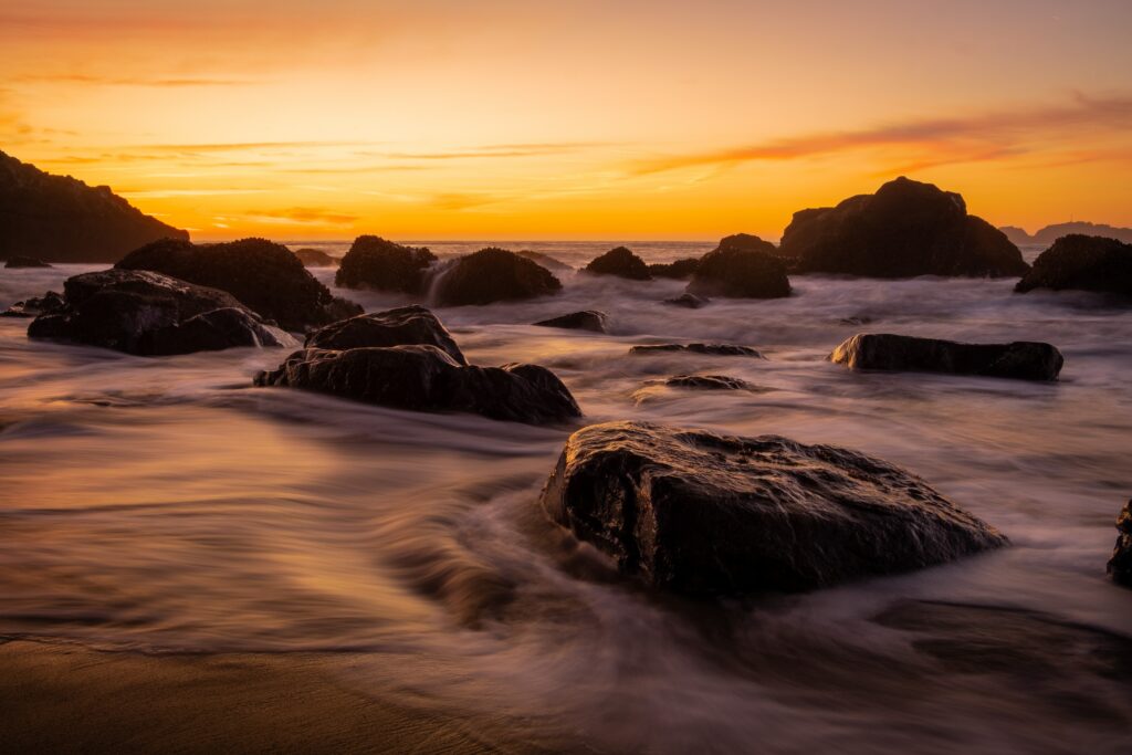 Smooth stones on serene coast at sunset with golden light and dramatic clouds wallpaper background
