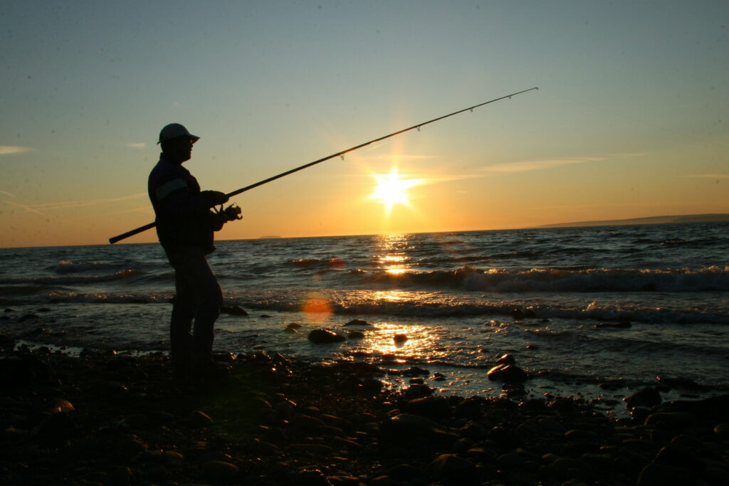 Serene Sunset Angler: Capturing Tranquility on Beachside Waters Wallpaper