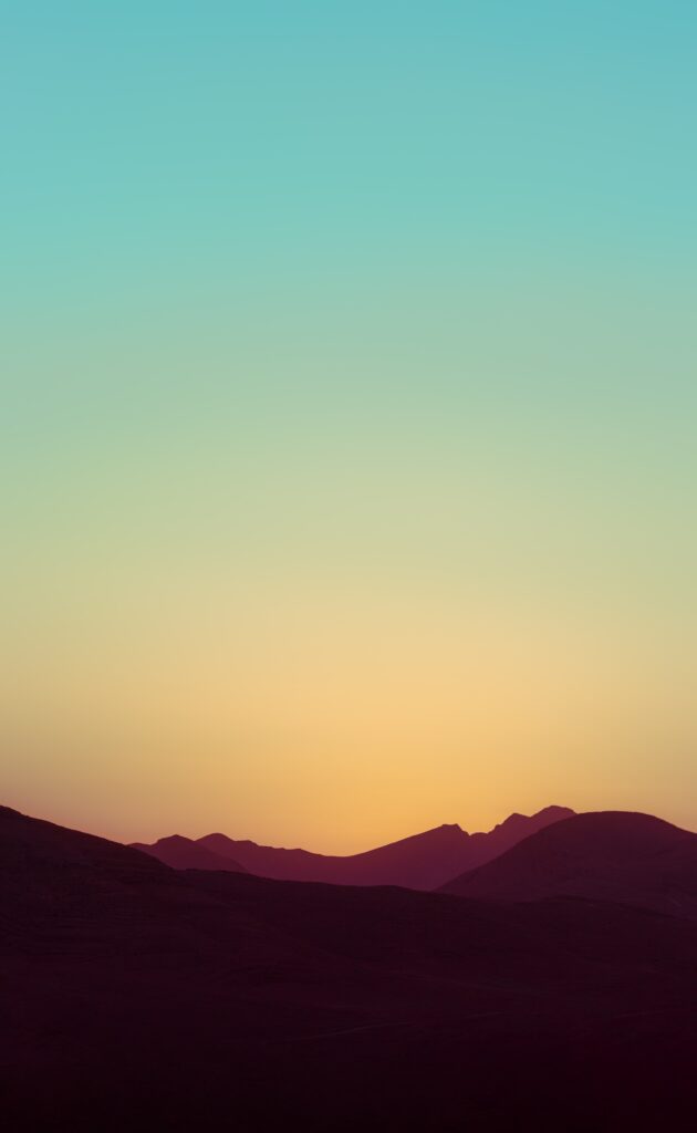 Serene hills silhouette at sunset with warm orange and yellow sky fading into blue gradient wallpaper