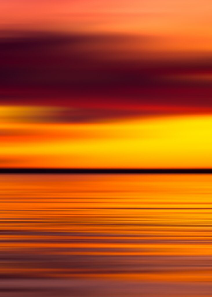 Sunset wallpaper with vibrant orange yellow and red sky reflecting on calm smooth water horizon