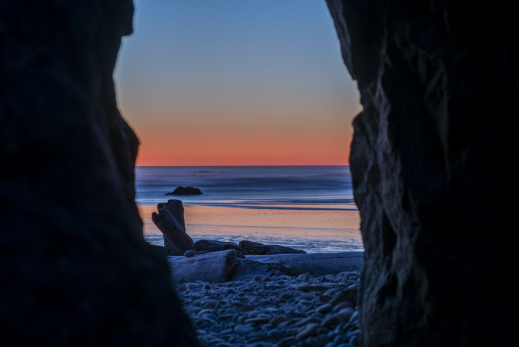 Sunset horizon viewed from cave with orange pink skies smooth pebbles calm blue sea background Wallpaper