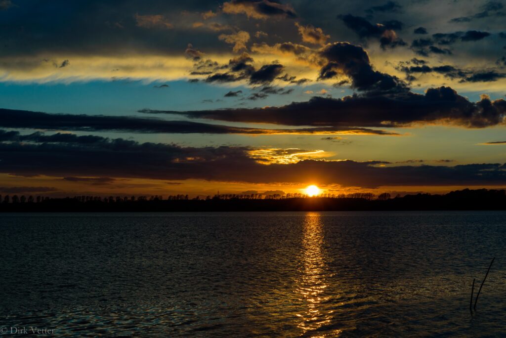 Tranquil lake reflecting golden sunset hues with dark clouds and gentle ripples at dusk wallpaper