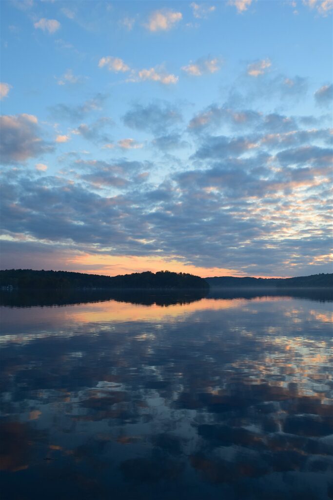 Tranquil lake at vibrant sunset reflecting pastel clouds and serene sky with mirrored water patterns Wallpaper