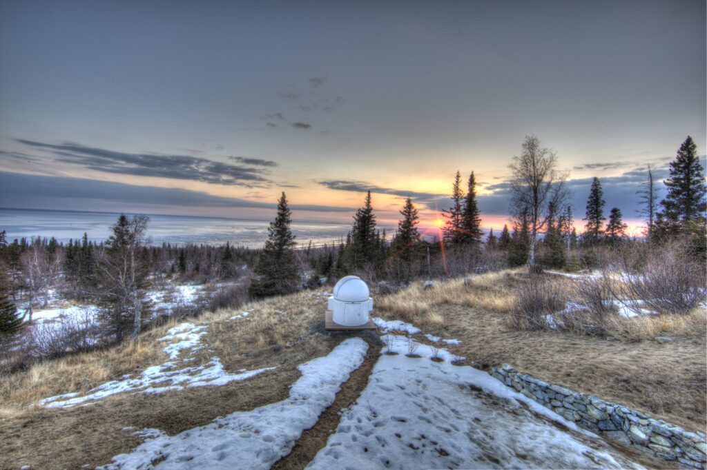 Sunset over snowy field with pine trees and distant observatory dome serene landscape wallpaper