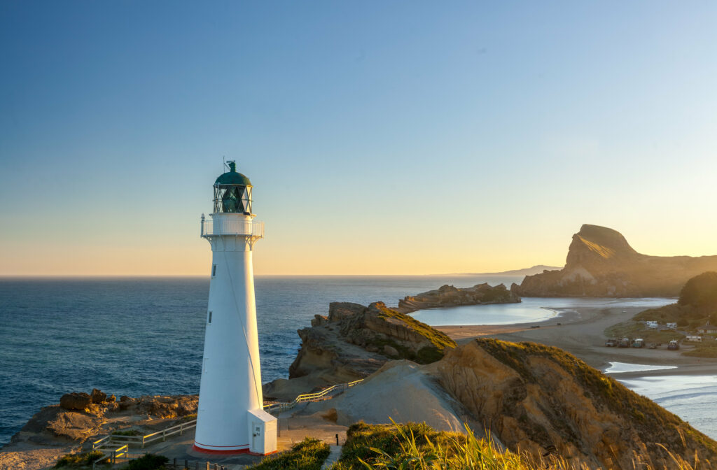 White lighthouse by blue ocean at sunset with coastal cliffs peaceful scenic wallpaper background