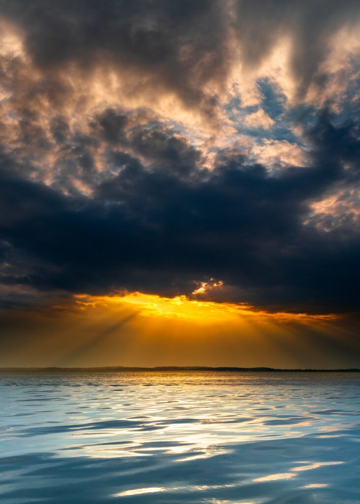 Breathtaking sunset over calm lake with golden sunlight and dramatic textured clouds reflection Wallpaper