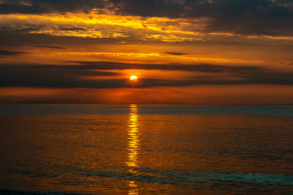 Sunset over calm sea with golden light and dramatic clouds creating serene wallpaper background