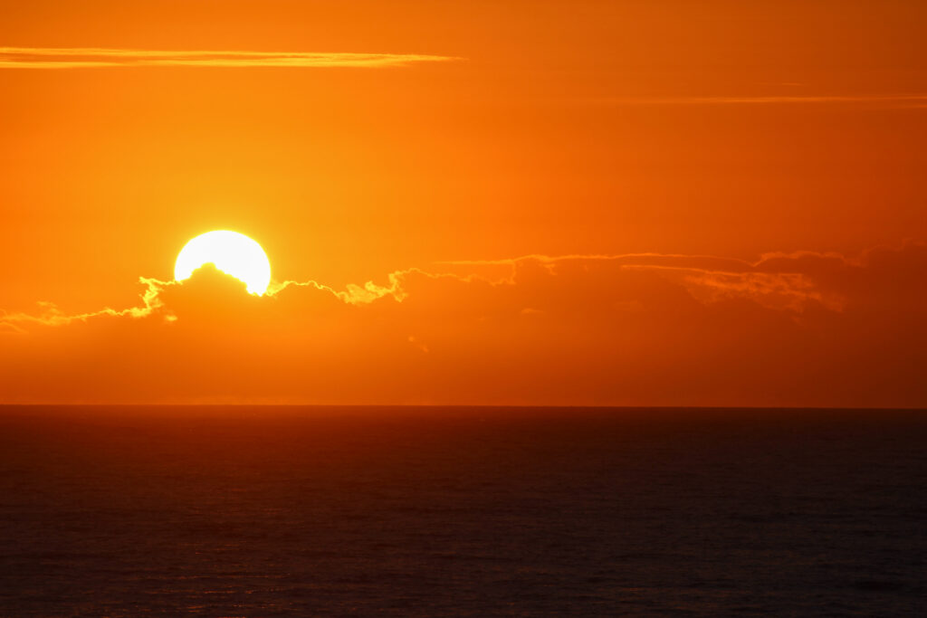 Sunset wallpaper with glowing sun behind clouds casting warm orange and golden hues over calm sea