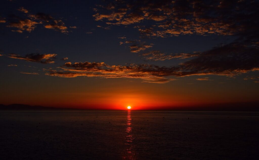 Sunset over calm sea with glowing orange sun and dramatic warm clouds in twilight sky wallpaper