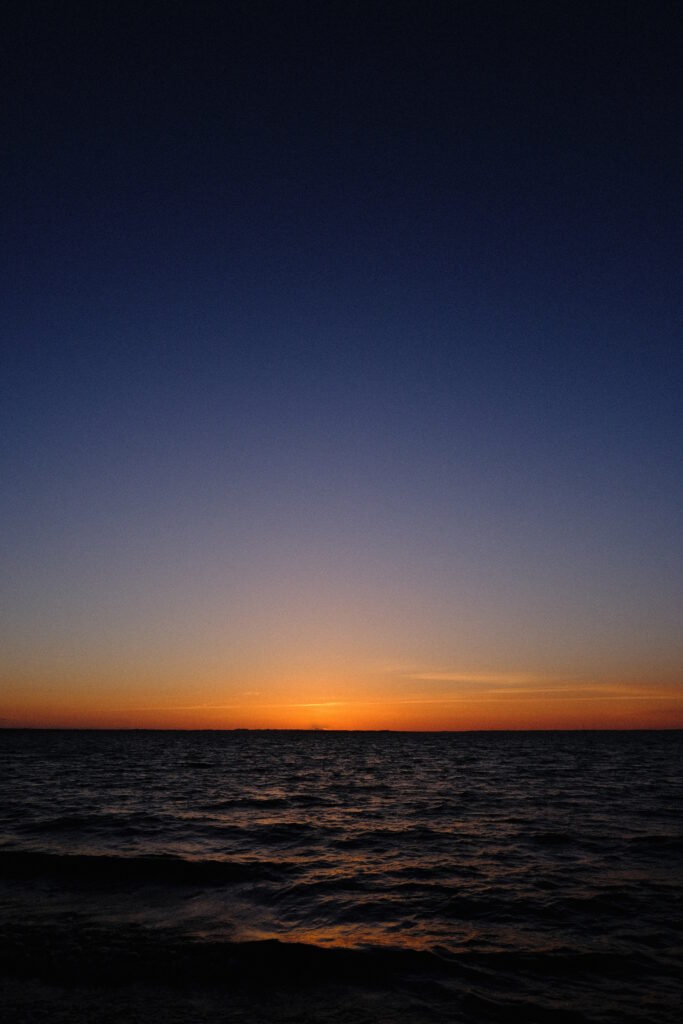 Serene sea horizon at sunset with warm orange and deep blue sky minimalist calming wallpaper
