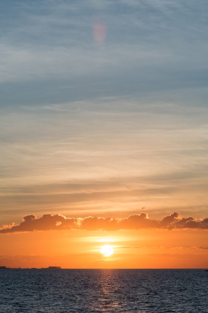 Serene sunset wallpaper with glowing sun over calm sea and soft orange yellow blue sky gradients