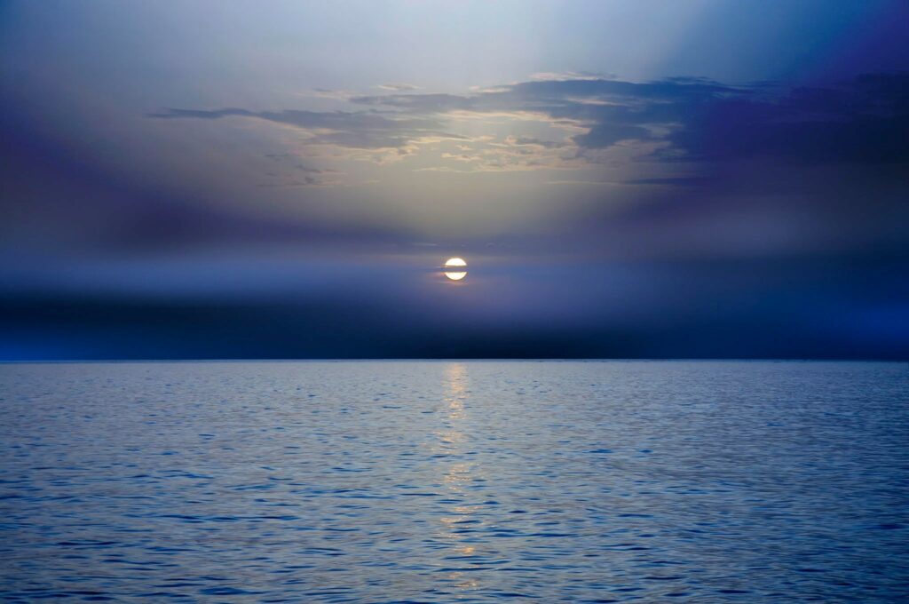 Calm sea sunset wallpaper with dark clouds vibrant blue purple sky and shimmering reflections