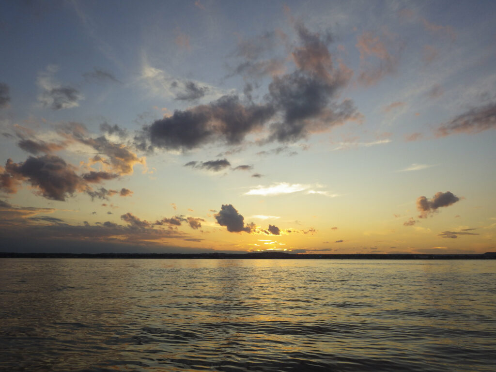 Serene sunset over calm sea with golden orange hues and soft illuminated clouds wallpaper background