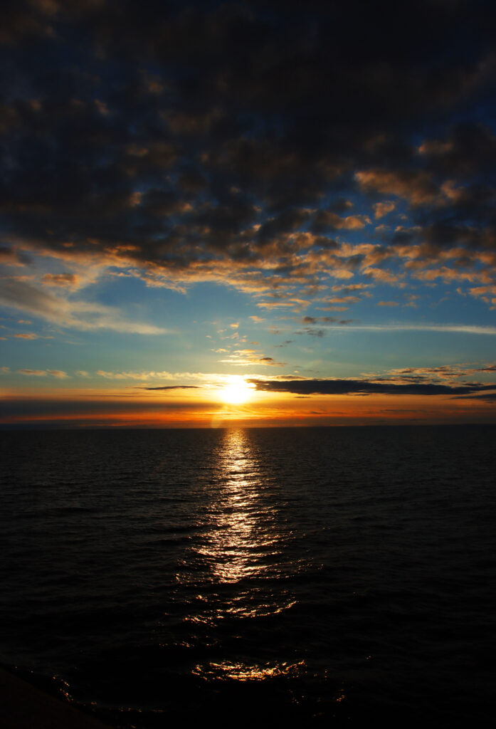 Serene sea sunset wallpaper with golden sun dipping below horizon and dramatic cloud sky