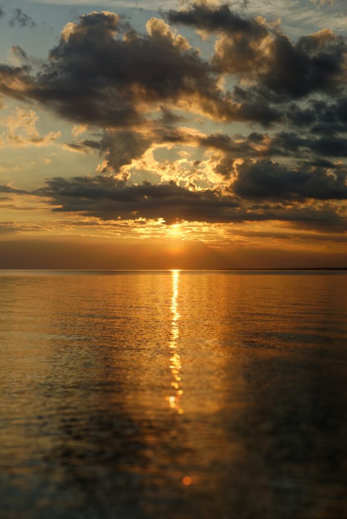 Serene sunset over calm sea with golden sunlight reflections and dramatic clouds wallpaper background