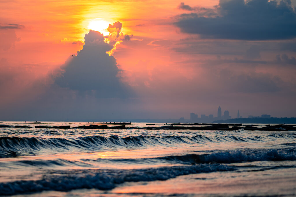 Serene sunset over calm sea with golden sunlight filtering through dramatic clouds wallpaper