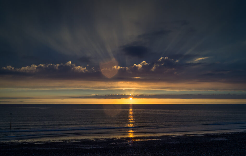 Serene sea sunset wallpaper with golden rays calm water deep blue sky and warm orange clouds