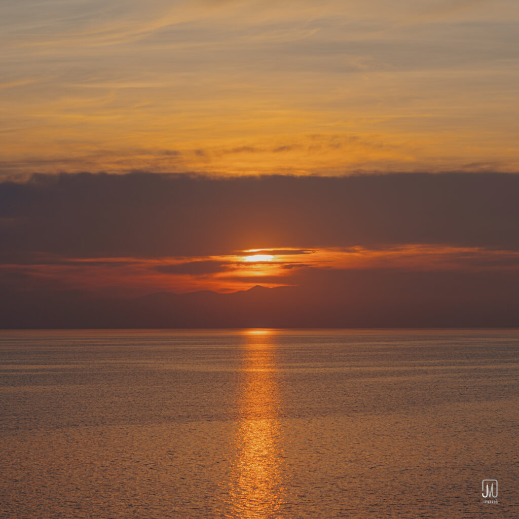 Serene sunset over calm sea with orange and gold reflections and distant silhouette horizon wallpaper