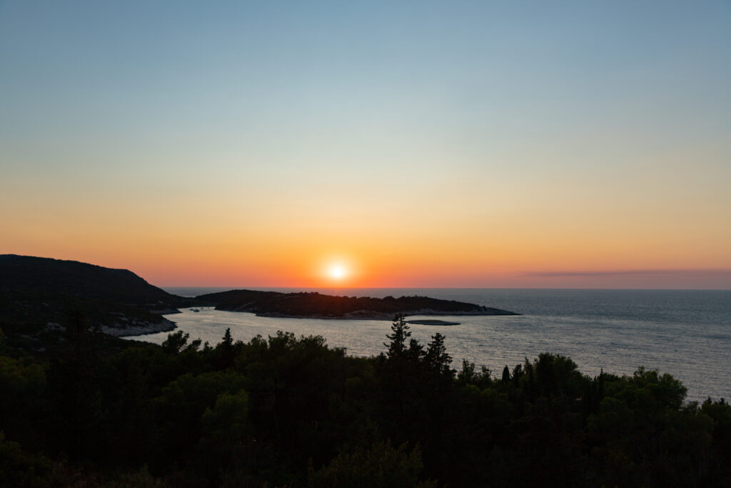 Serene sea sunset wallpaper with orange gold sky reflecting on calm water and lush island view
