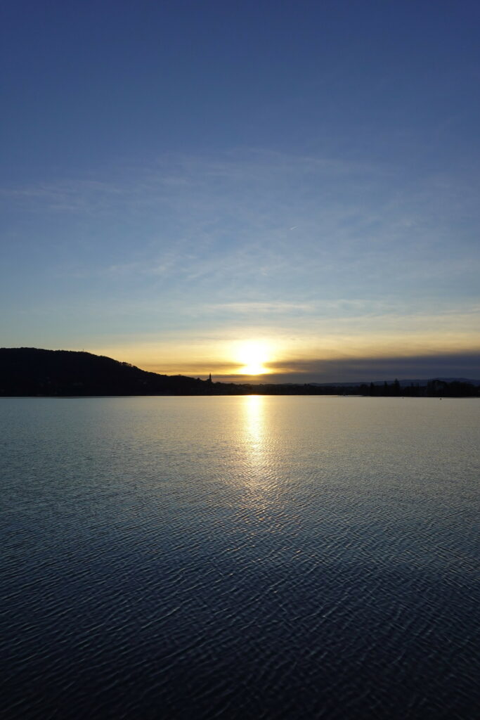 Serene sunset over calm water with golden reflection and silhouetted hills at dusk wallpaper