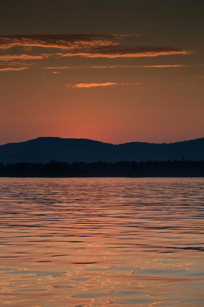 Serene sunset wallpaper with calm water waves orange purple sky and dark mountain silhouette background
