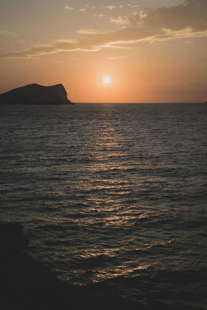 Serene sunset over calm water with golden reflection and silhouetted rocks wallpaper background