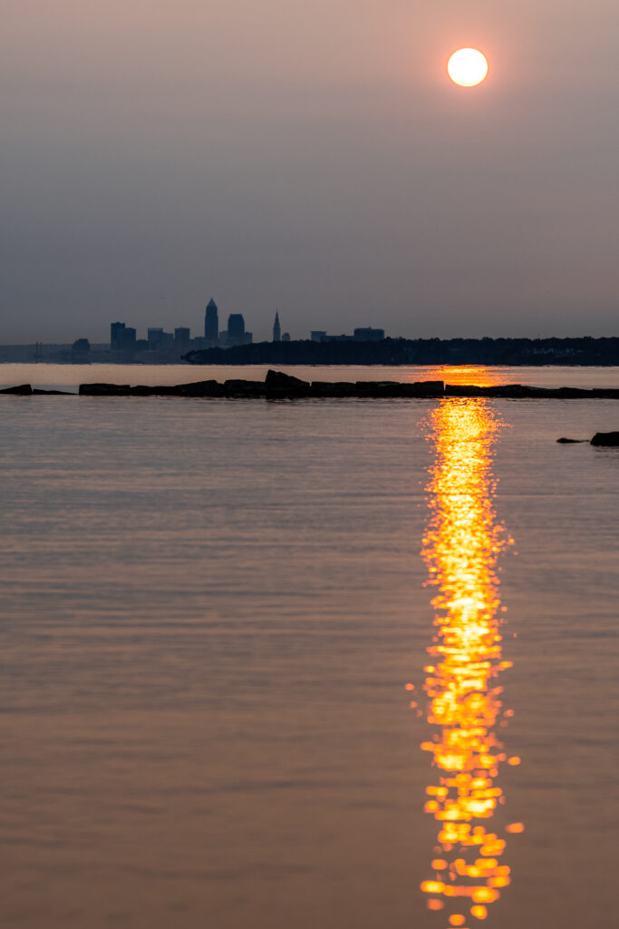 Serene sunset over calm waters with city silhouette warm orange sky peaceful wallpaper background