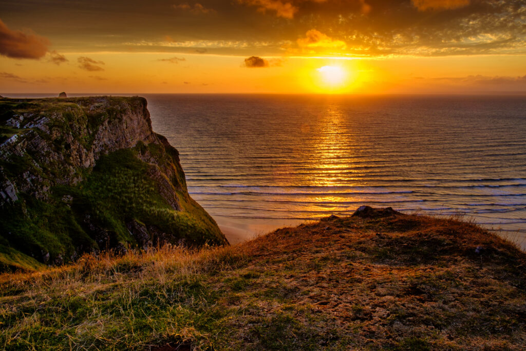 Sunset over calm water with golden light and green grassy cliffs creating serene landscape wallpaper