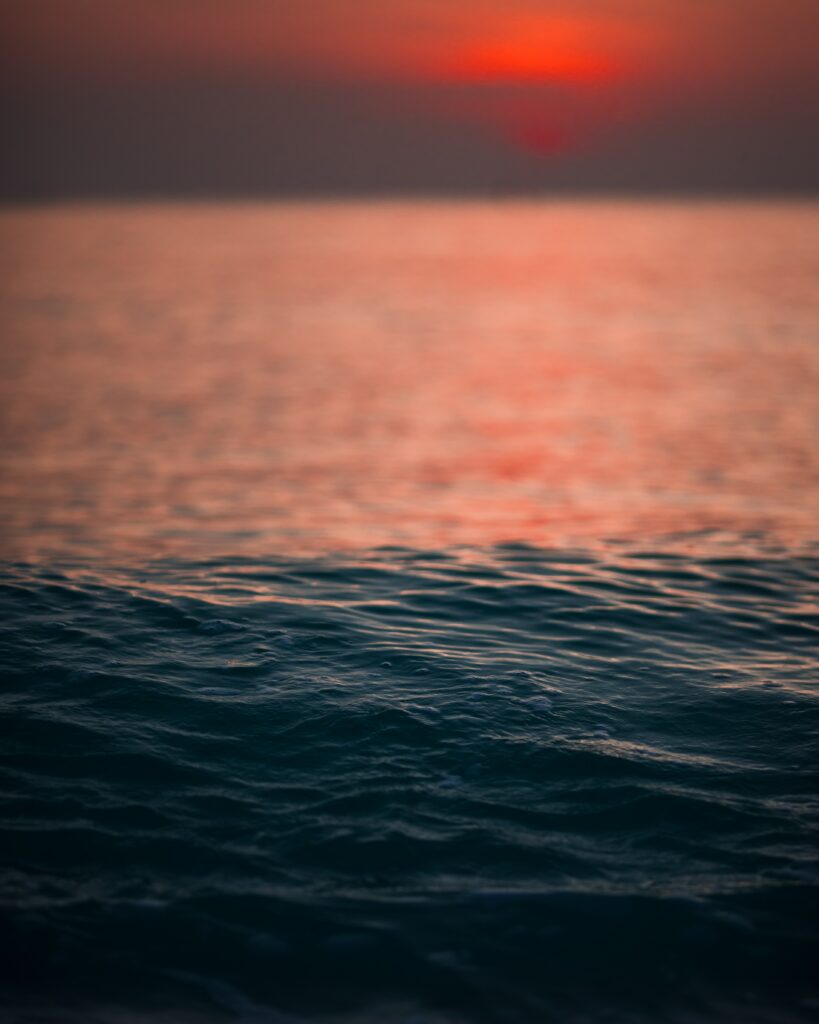 Serene sea water ripples under vibrant orange red sunset sky wallpaper background peaceful view