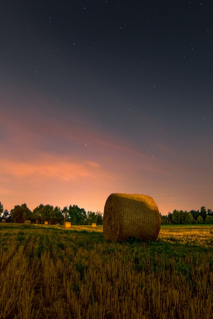 Haystack at sunset in a peaceful rural field with golden grass and a colorful twilight sky Wallpaper
