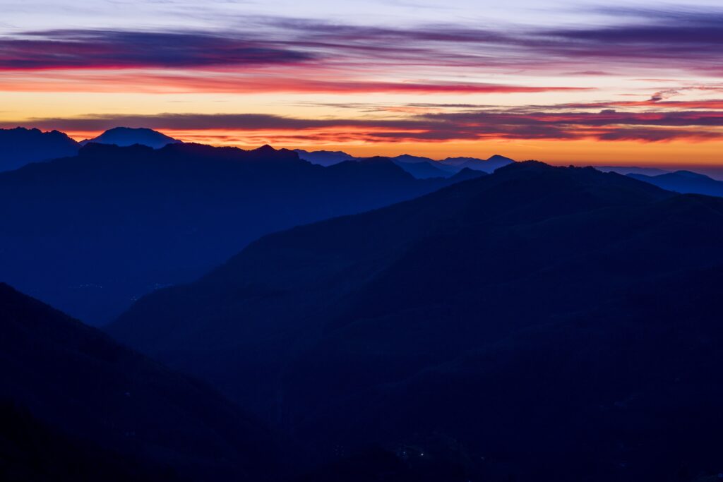 Sunset over layered mountain ridges with vibrant orange pink sky and deep blue purple shadows Wallpaper