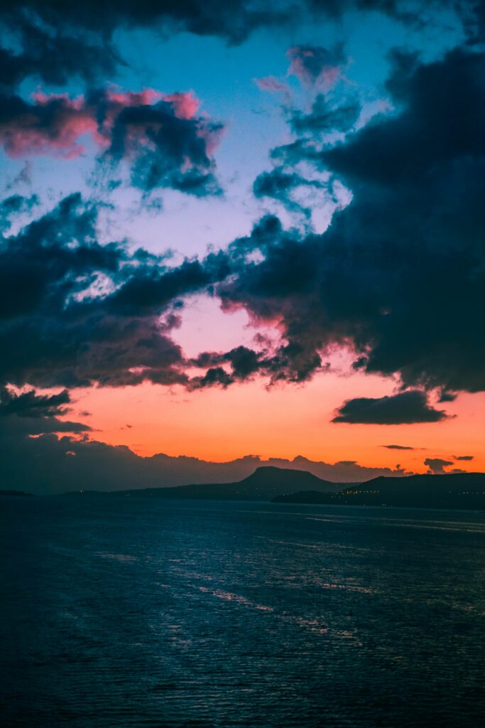 Sunset over mountains with dark clouds and colorful sky reflecting on calm sea wallpaper background