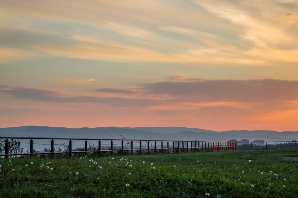Sunset over Petrovaradin Novi Sad grassy field dandelions fence hills peaceful countryside wallpaper