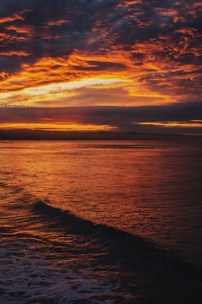 Sunset over reflective water with gentle waves vibrant orange red sky serene seascape wallpaper