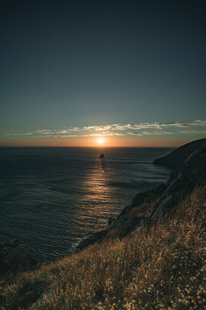 Sunset over sea with glowing sun reflecting on water rocky slopes and grass coastal wallpaper.jpg
