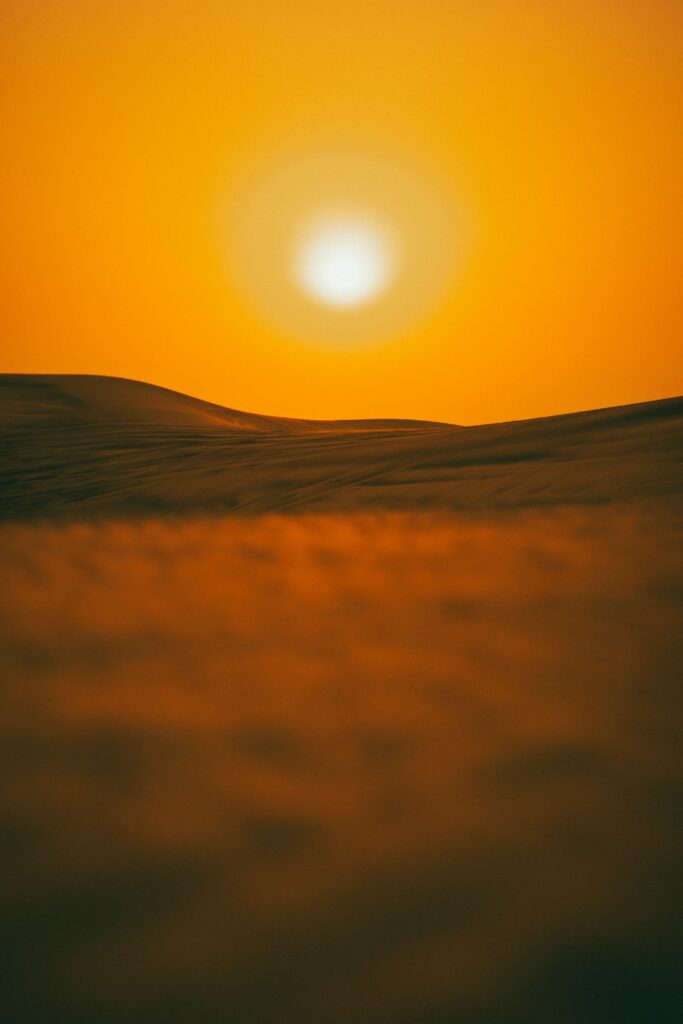 Serene sunset over rolling desert hills glowing sun warm orange sky golden sand textures background Wallpaper